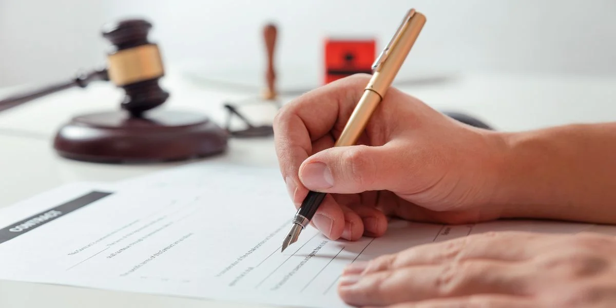 Person signing a contract with a fountain pen next to a gavel and notary stamp